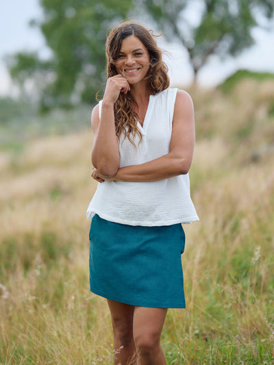 Woman in a white sleeveless top and teal skirt RipSkirt standing in a field with trees in the background